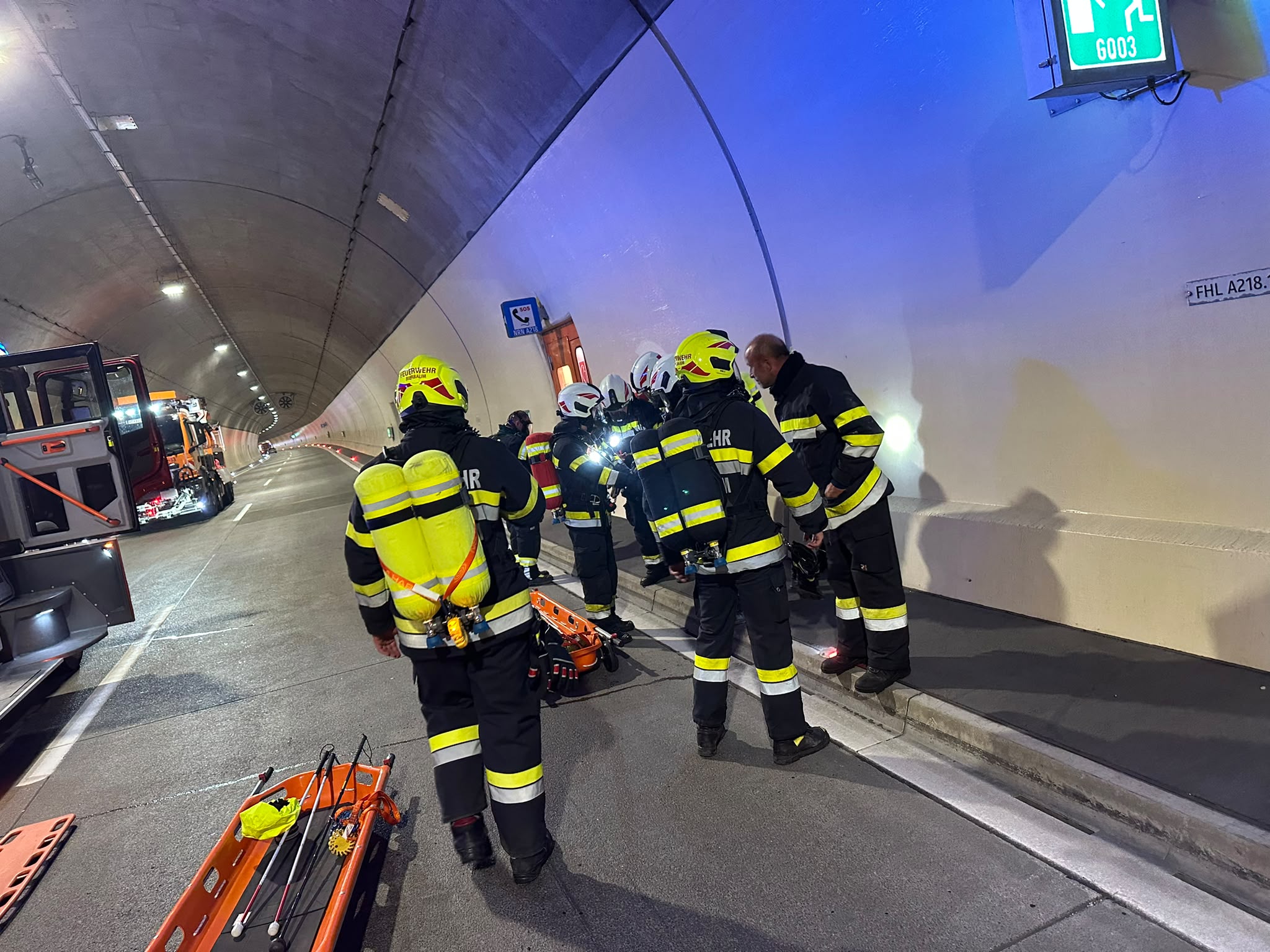 Feuerwehrleute im Tunnel mit Tragen und Einsatzfahrzeugen im Hintergrund